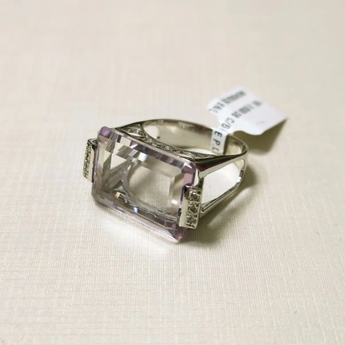LOTE 002 - Um anel, em ouro branco, com uma pedra de quartzo lilás, retangular, seis pedras de diamantes nas laterais