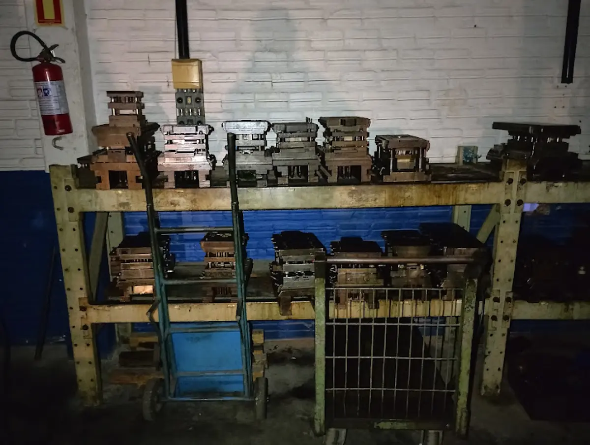 LOTE 176 - Lote composto por dezenas de moldes e matrizes metálicas industriais (corte, repuxo e estamparia) de variados tamanhos e formatos; estruturas e estantes de aço industriais para armazenagem; 01 carrinho manual de movimentação de carga; e conjunto de componentes de ferramentaria soltos sobre bancada (pinos guia, molas de compressão, punções e blocos de aço).