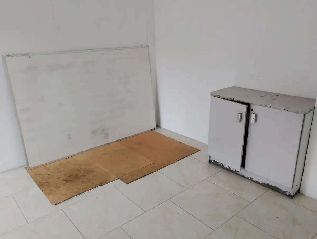 LOTE 132 - 01 mesa de escritório em "L" branca com 02 cadeiras, 01 equipamento (aparenta ser impressora/relógio ponto), 02 quadros brancos, 01 armário baixo de duas portas e 01 bancada/mesa de apoio branca.