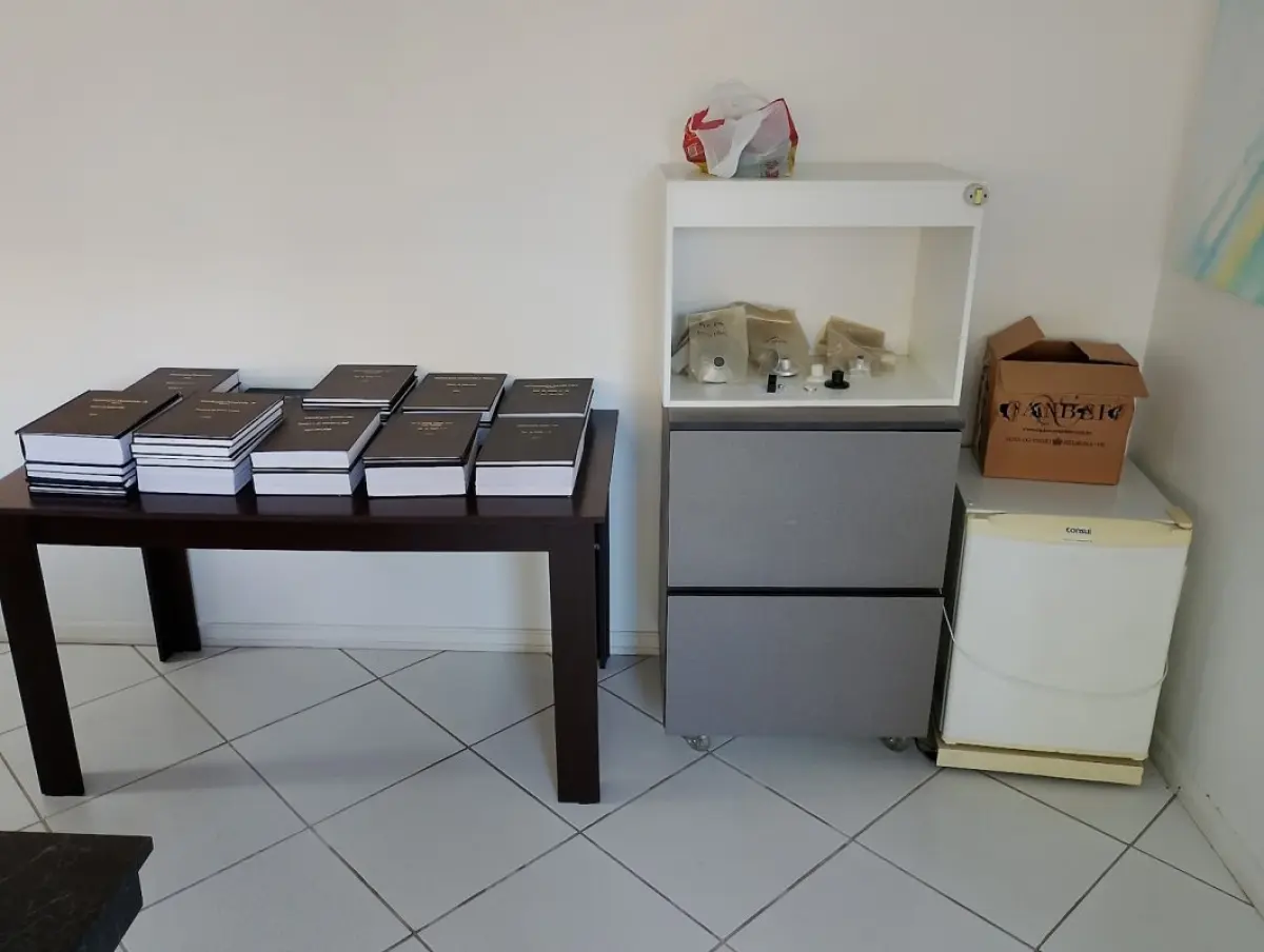 LOTE 202 - Lote corporativo completo contendo: Estrutura de copa com balcão planejado em 'L' com pia de inox, 04 banquetas altas, 02 frigobares Consul, 02 purificadores de água (Soft/Coluna) e 01 cafeteira Saeco; Mobiliário de escritório com 01 mesa diretiva curva com tampo de vidro e cadeira presidente branca, 01 mesa de reunião com tampo de vidro (06 lugares) com 06 cadeiras brancas estruturais, 01 mesa de reunião preta grande (18 lugares), 02 mesas operacionais em 'L' com gaveteiros, 03 mesas retas, 01 arquivo de aço com 04 gavetas, armários, balcões com chaves, 02 estantes expositoras grandes com prateleiras de vidro, 01 mesa de centro, 02 gaveteiros volantes e 12 cadeiras universitárias pretas; Estofados com 02 sofás modulares de canto grandes (01 branco e 01 marrom) e 05 poltronas pretas; Eletrônicos com 01 Smart TV LG, 01 TV Sony, 04 monitores (Samsung/AOC), 02 impressoras e central técnica de som (Orion/Proton/Philips); Itens diversos com lousa branca, suporte para TV, caixas de arquivo e mostruário de calçados contendo malas de rodízio (Renus/Alyssa), calçados (Pegada/Modare) e caixas