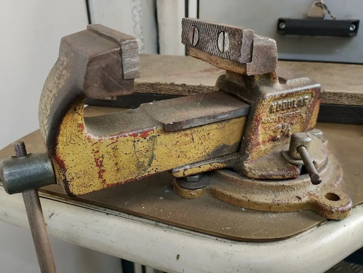 LOTE 111 - 01 bancada de trabalho ergonômica (estilo ferramenteiro/ourives) com estrutura em perfil de alumínio, tampos com recorte e apoios para os pés, 01 morsa de bancada marca Schulz nº 2, 01 morsa de bancada marca Modular nº 2 1/2, 01 luminária articulada, 01 cadeira giratória alta, pequeno lote de lixas, organizadores de madeira e miudezas em geral (nas gavetas).