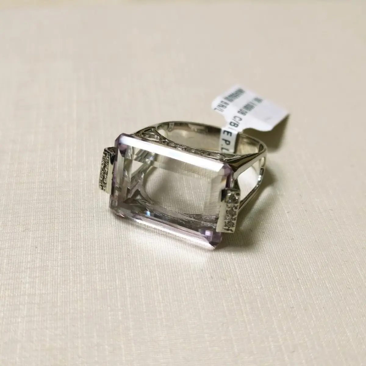 LOTE 002 - Um anel, em ouro branco, com uma pedra de quartzo lilás, retangular, seis pedras de diamantes nas laterais
