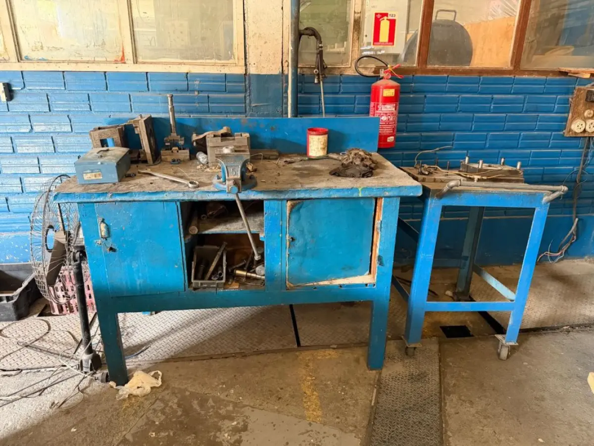 LOTE 251 - 08 estantes metálicas industriais de carga/almoxarifado; aprox. 80 caixas de papelão numeradas e bins plásticos com componentes industriais, ferragens e peças variadas; aprox. 09 bancadas de trabalho e mesas/escrivaninhas de oficina; 01 carrinho metálico de ferramentas com rodízios; 01 furadeira de bancada; aprox. 06 cadeiras operacionais e banquetas; 01 balança digital Toledo; aprox. 20 porta-moldes, matrizes e blocos pesados de metal; ferramentas manuais e elétricas diversas (morsa, esmerilhadeira, chaves)