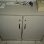 LOTE 012 - armário com 2 portas de abris e 2 prateleiras cor marrom e um banco de espera cinza