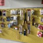 LOTE 042 - Lote com quador mostruario, silicone, linhas de nylon, serrote, martelo, disco de corte, pedra para retificas, regua, tesourão, mostra de modelos de parafusos, pedras de afiar, tampa de vaso, adaptador de mangueira, torneiras, trincha, rolo de pintura, capacetes de epi, oculos. 